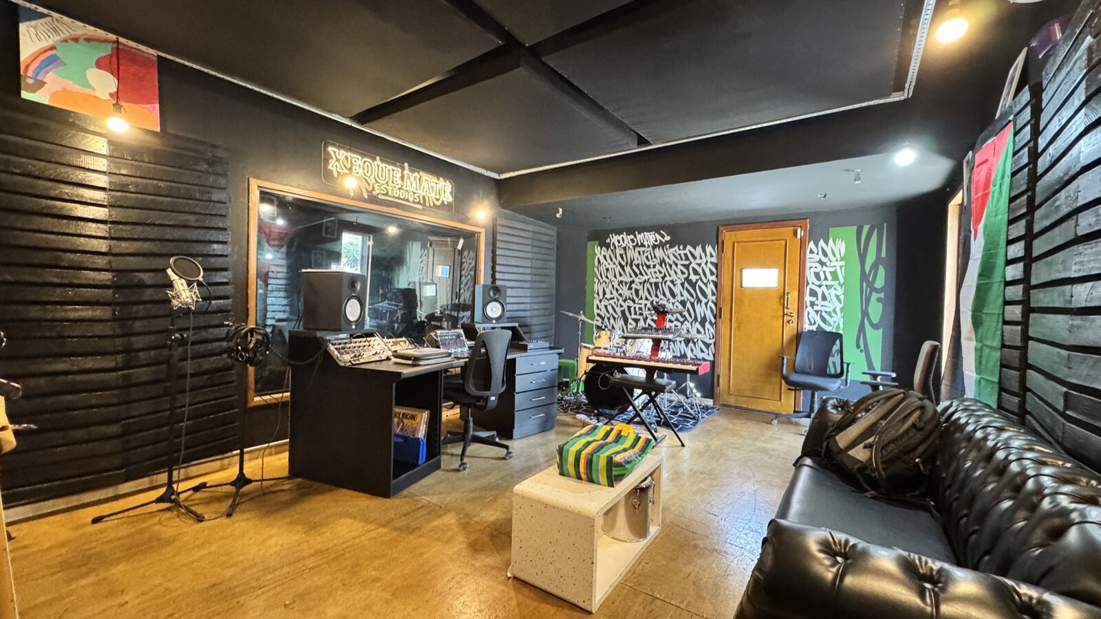 Sala de gravação do estúdio, com monitores, mesa e a parede pichada ao fundo